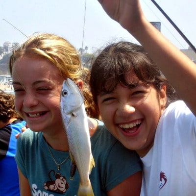 Two girlslaughing and fishing from Santa Monica Pier at Aloha Beach Camp Summer Camp