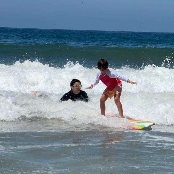 Camp director teaching a young boy how to surf in the ocean at Aloha Beach Camp.