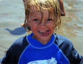 Young boy at Aloha Beach Camp's Keiki Camp Program in blue rashgaurd smiling with tounge out of his mouth